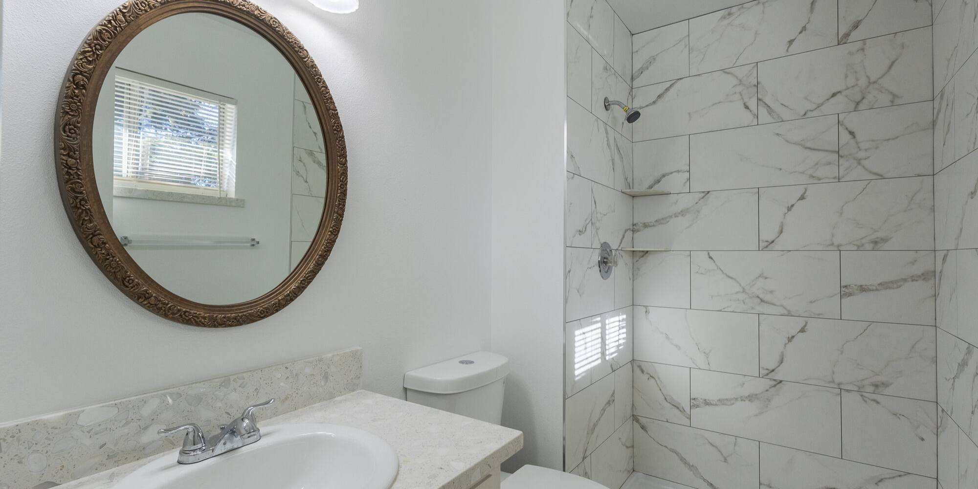 Modern walk-in shower with marble tile and round mirror vanity in a Reno home by M&G Construction.