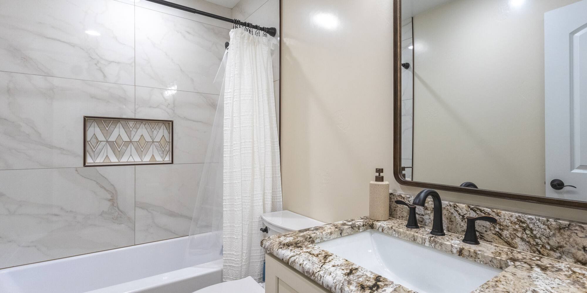 Updated tub shower with accent tile niche and granite vanity by M&G Construction in a Reno home.