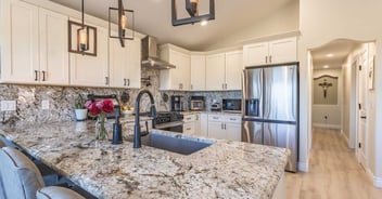 Image of kitchen remodel with large granite island, modern lighting, and white cabinetry in Reno, NV by M&G Construction