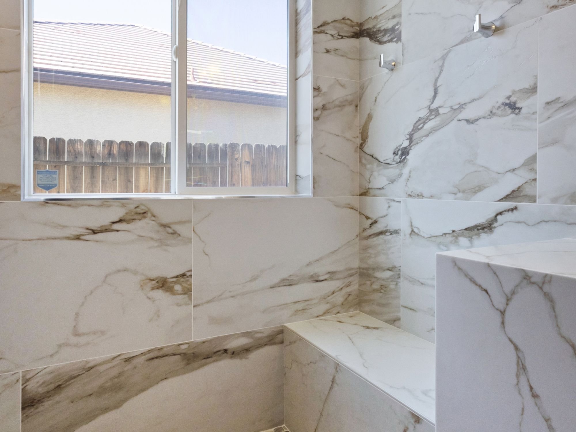 A dedicated dry-off area in a Northwest Reno bathroom remodel by M&G Construction with tiled walls, towel hooks, and a window