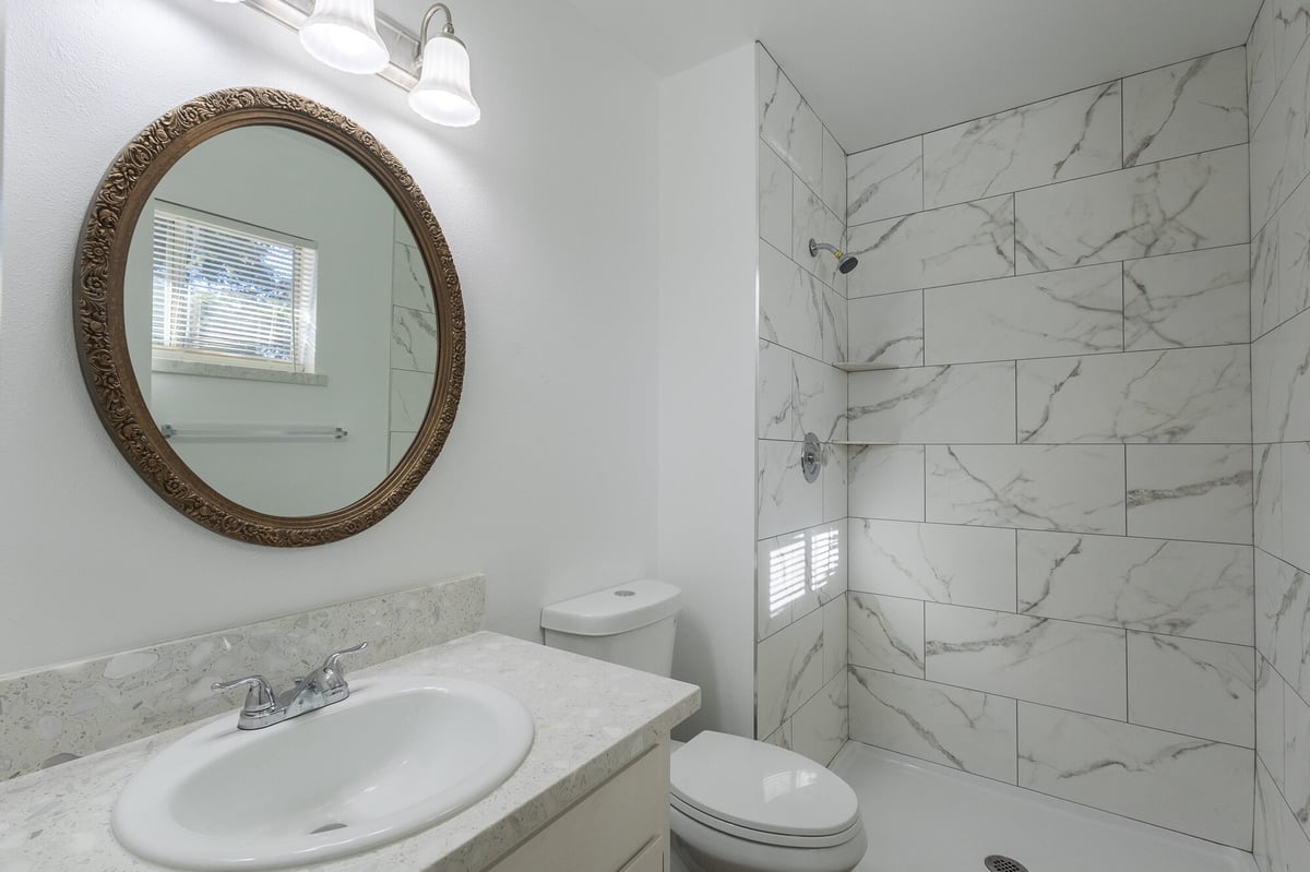 Modern walk-in shower with marble tile and round mirror vanity in Reno custom home by M&G Construction.