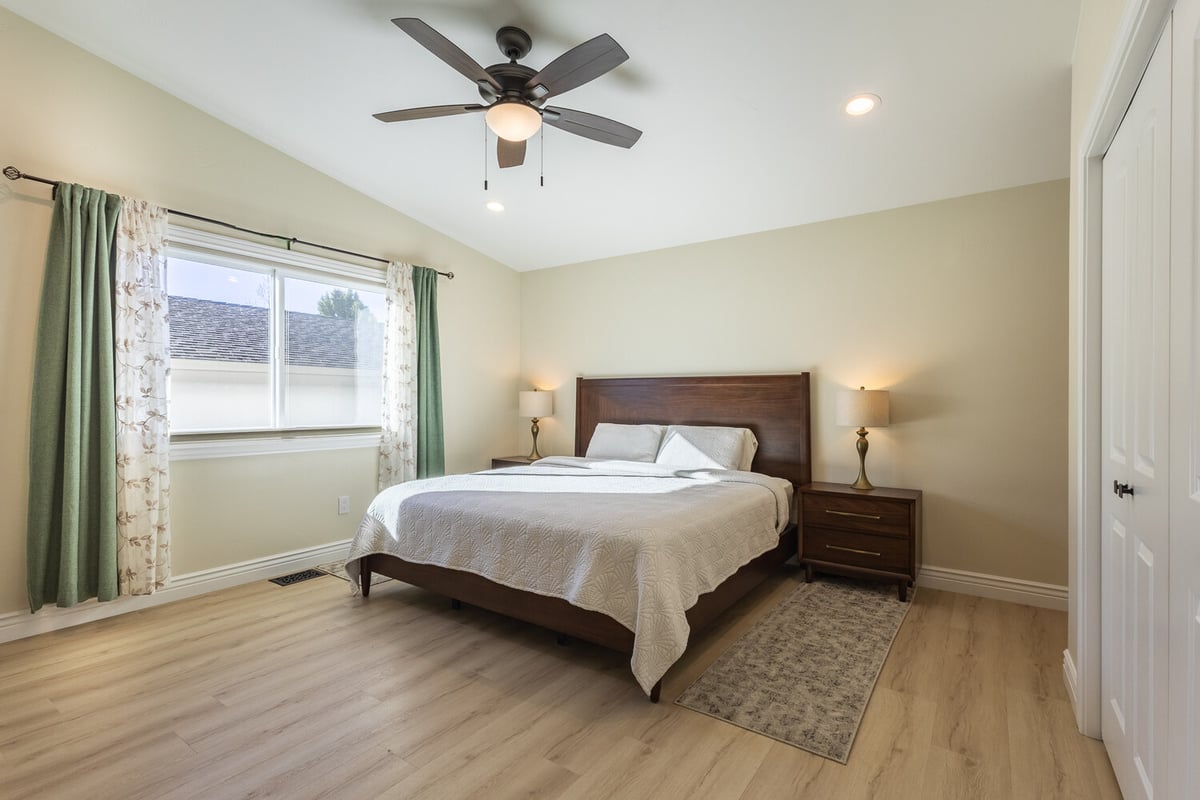 Elegant bedroom with wood furnishings, white bedding, and ceiling fan in M&G Construction custom home, Reno, NV.